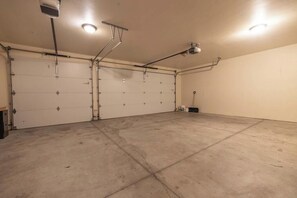 A spacious garage with two large garage doors, overhead lighting, and visible plumbing. - Golden Oak Estate | 7BR Luxury. Wine Room. Views. (Big Bear Lake)