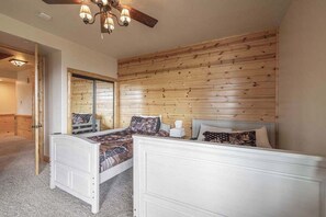 A bedroom with two beds, a wooden headboard, a ceiling fan, and a mirror. - Golden Oak Estate | 7BR Luxury. Wine Room. Views. (Big Bear Lake)