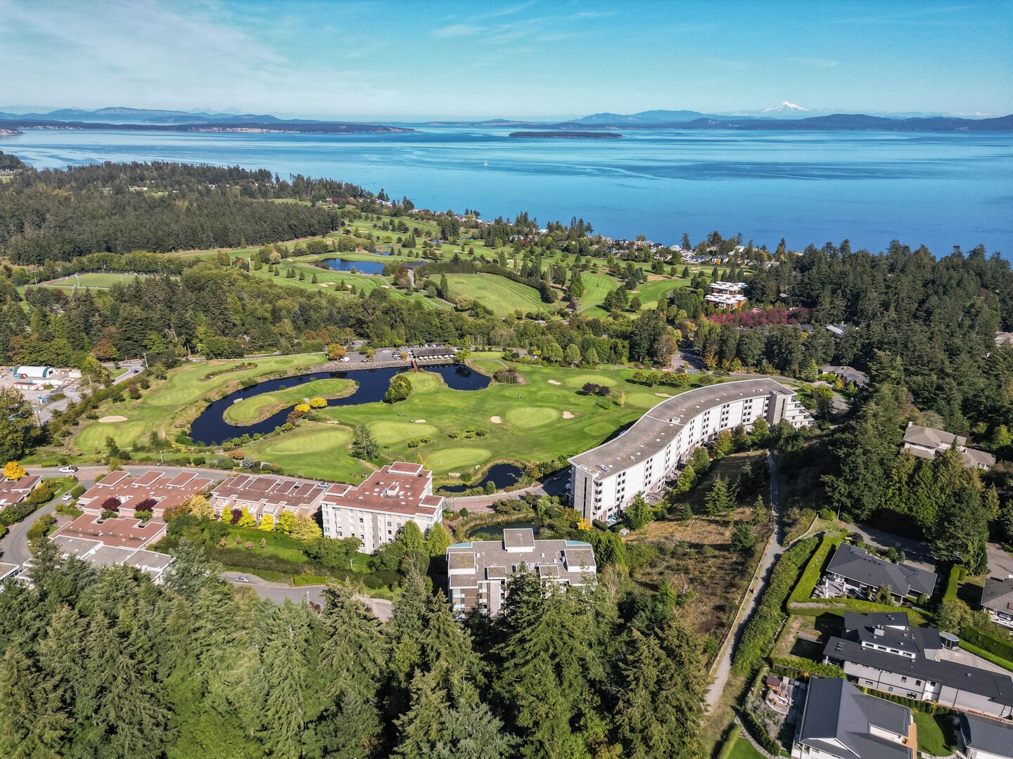 En vy över en golfbana från ovan, med ett stort byggnadskomplex omgivet av tät skog och en sjö eller ett annat vattendrag.