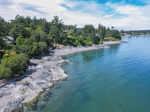 A coastal landscape with a rocky shoreline, dense greenery, and a clear blue sky.