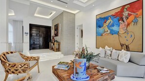 A modern living room with a sofa, a wooden coffee table, a wicker chair, and a large abstract painting. - The Rainbow (Miami)