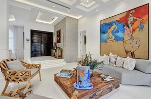 A modern living room with a sofa, a wooden coffee table, a wicker chair, and a large abstract painting. - The Rainbow (Miami)