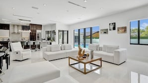 A modern living room with a white sofa set, a coffee table, and a view of a swimming pool. - The Rainbow (Miami)