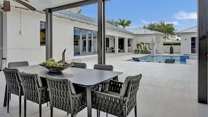 A modern patio with a dining table and chairs, a ceiling fan, and a view of a swimming pool. - The Rainbow (Miami)