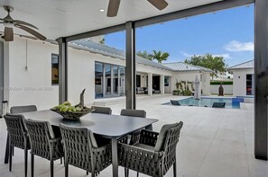 A modern patio with a dining table and chairs, a ceiling fan, and a view of a swimming pool. - The Rainbow (Miami)