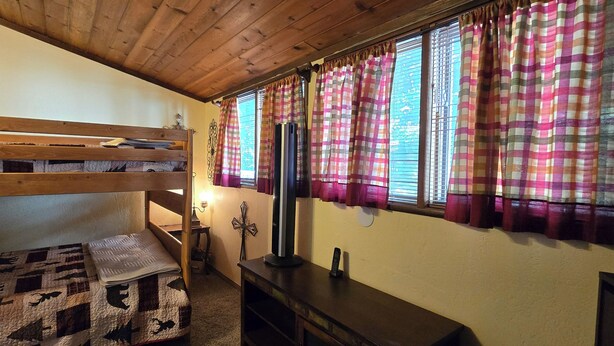 A bunk bed room with a quilt, a TV, and a window with curtains. - Crestline Mountain Retreat (Crestline)