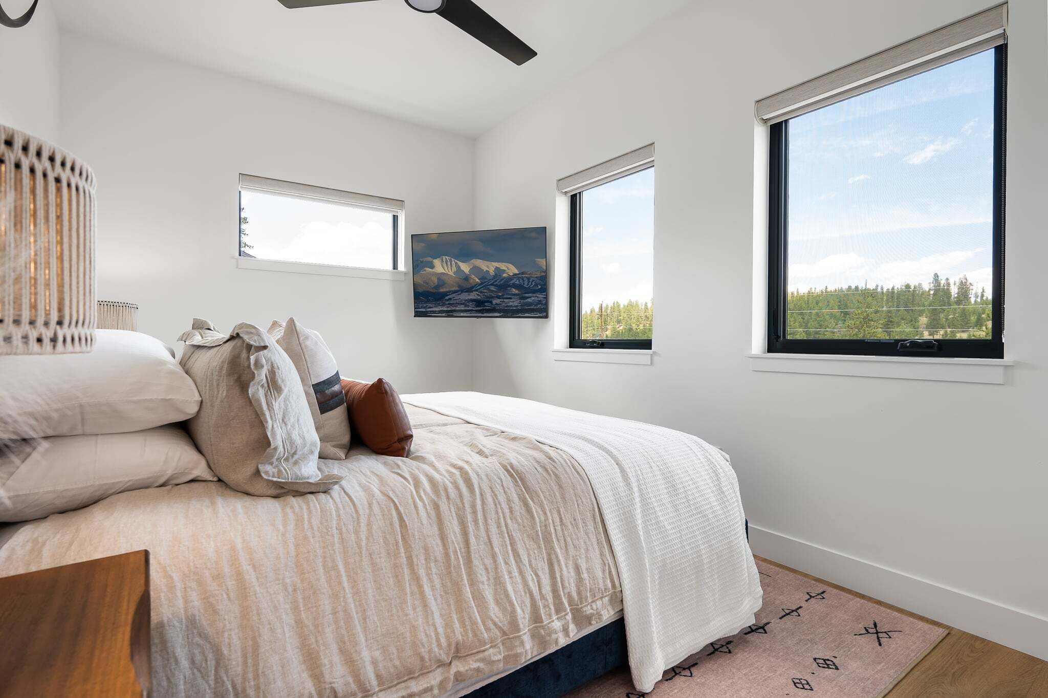 A bedroom with a bed, a ceiling fan, a painting, and large windows.