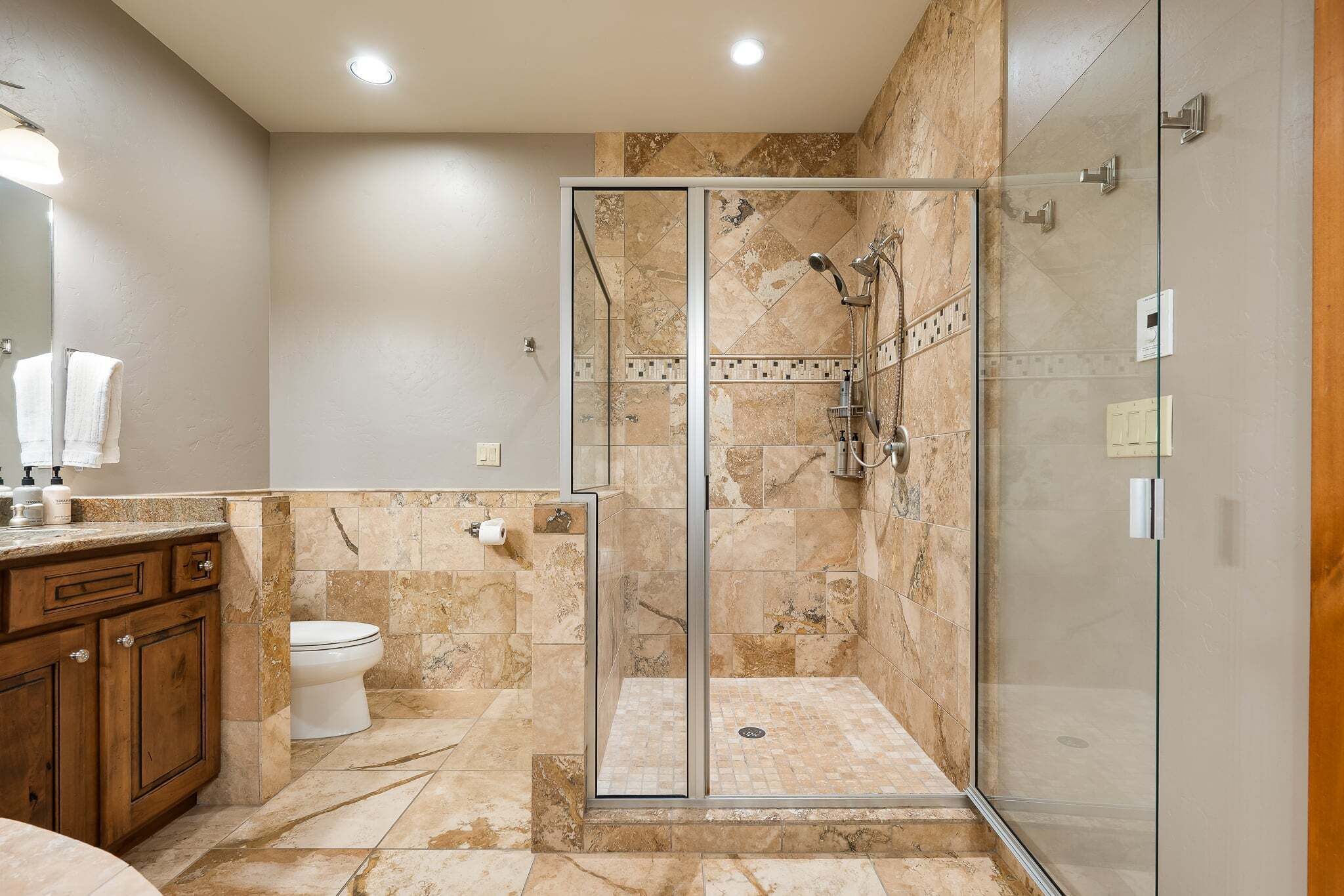Un baño moderno con cabina de ducha de vidrio, suelo de baldosas de mármol y tocador de madera.