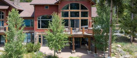 A large, multi-story house with a prominent balcony, stone chimney, and a well-maintained garden.