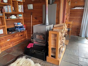 A cozy room with a wood-burning stove, a bookshelf, and a fireplace mantel. - Kereru Lodge Kakahi, private and peaceful getaway (Kakahi)