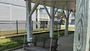 A wooden swing bench under a covered area with a metal fence in the background. - 3 Bedroom home with access to the canal! (Supply)