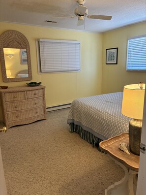 Un dormitorio con cama, cómoda, espejo, ventilador de techo y ventana con persianas.