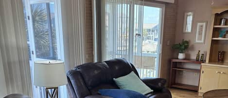 A living room with a leather sofa, a wooden coffee table, and a view through large windows.