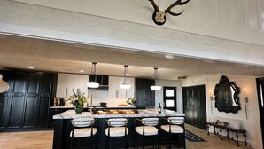 Een moderne keuken met een groot eiland, donkere kastjes, hanglampen en een opgehangen geweih.