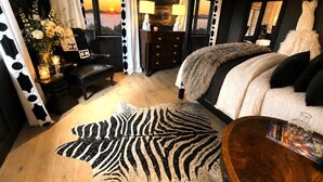 Een slaapkamer met een bed, een stoel, een kaptafel, een lamp, een vaas met bloemen en een zebra vloerkleed.