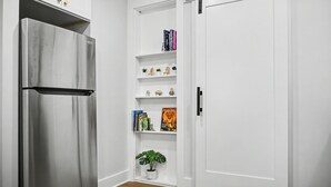 Eine Küche mit einem Edelstahl-Kühlschrank, weißen Schränken und einem Schiebetürenschrank mit Regalen, auf denen Bücher und Dekorationen stehen.