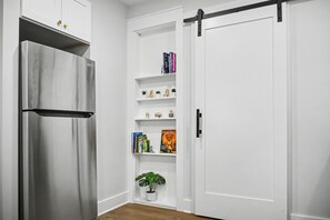 Eine Küche mit einem Edelstahl-Kühlschrank, weißen Schränken und einem Schiebetürenschrank mit Regalen, auf denen Bücher und Dekorationen stehen.