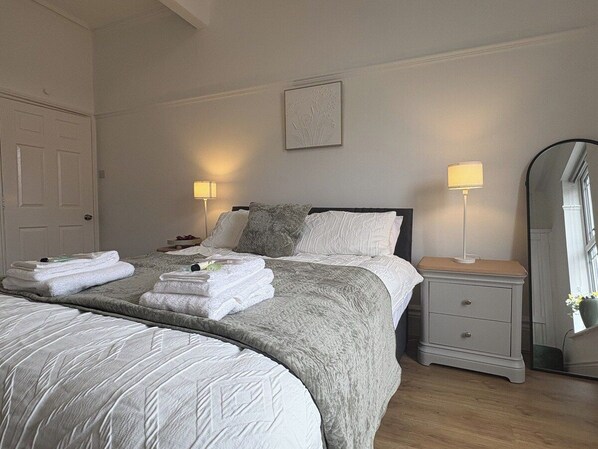 Ein Hotelzimmer mit einem großen Bett, zwei Nachttischen, einem Spiegel und einer Tür.