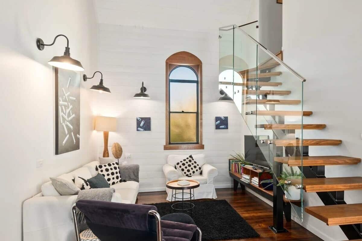 Un salon moderne avec un escalier en verre, des murs blancs et un mobilier minimaliste.