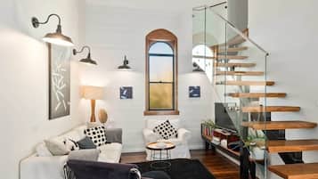 A modern living room with a glass staircase, white walls, and minimalist furniture.