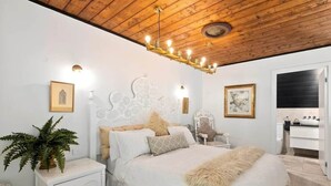 A bedroom with a wooden ceiling, a white bed with a fluffy blanket, a nightstand with a plant, and a white cabinet. - Church Conversion @ 39 Hoddle Street (Robertson)