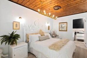 A bedroom with a wooden ceiling, a white bed with a fluffy blanket, a nightstand with a plant, and a white cabinet. - Church Conversion @ 39 Hoddle Street (Robertson)
