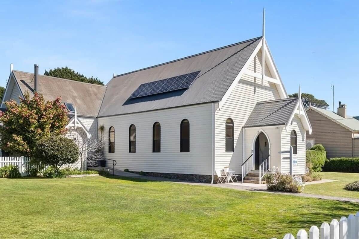 A white building with a sloped roof, a solar panel, and a small porch with steps.