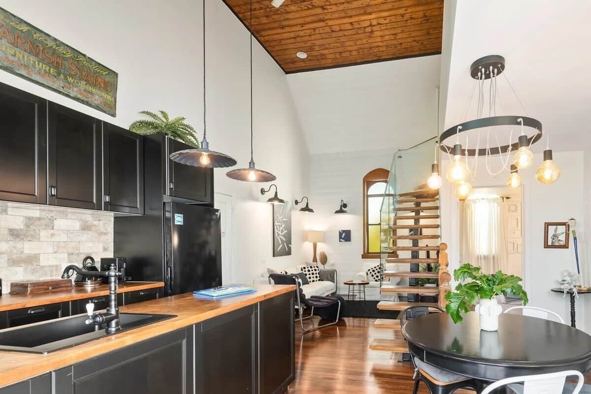 A modern kitchen with a wooden island, black cabinets, and pendant lighting.