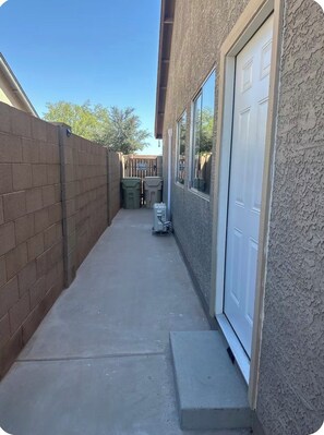 A narrow concrete pathway leading to a garage door, flanked by a brick wall and a stucco wall. - Cozy 1-bedroom townhome in adorable Glendale with AC (Glendale)