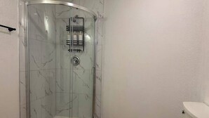 Un bagno con doccia vetro-muraria, un water e un pavimento in marmo.