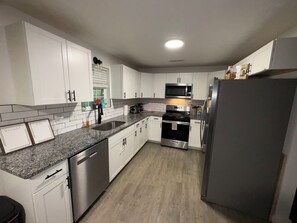 A modern kitchen with white cabinets, a granite countertop, stainless steel appliances, and a wooden floor. - The Ozark Gathering Place Spacious Family Retreat Near Springfield & Branson (Ozark)