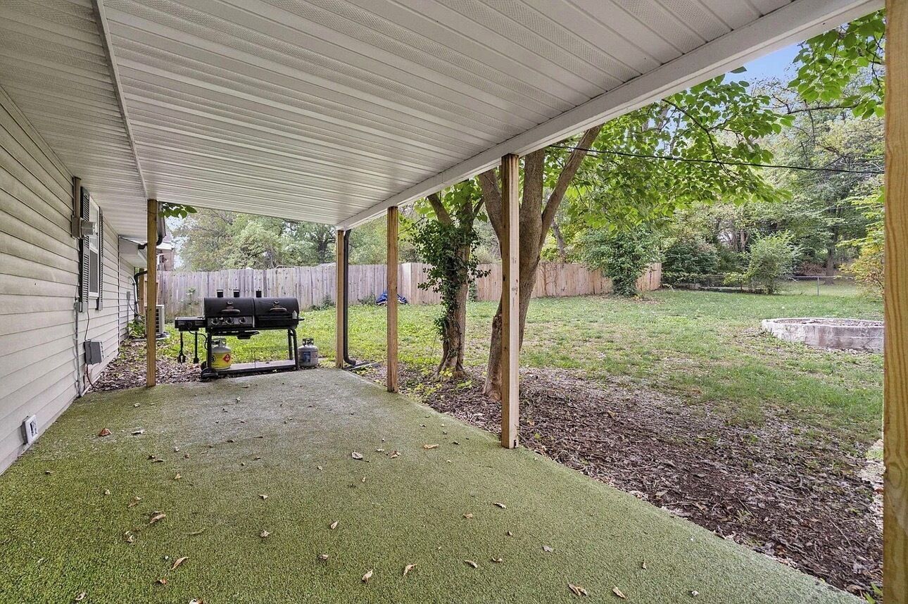 Un patio couvert avec un barbecue, une clôture en bois et une cour gazonnée.