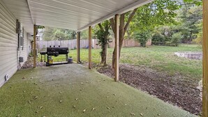 Un patio cubierto con una parrilla, una cerca de madera y un césped.