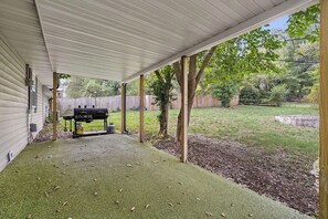Ein überdachter Patio-Bereich mit Grill, Holzzaun und Rasenfläche.