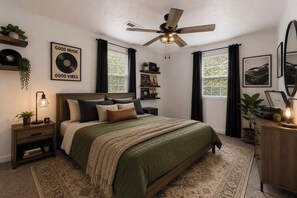 A bedroom with a bed, a ceiling fan, a nightstand, a dresser, a mirror, and a window with curtains.