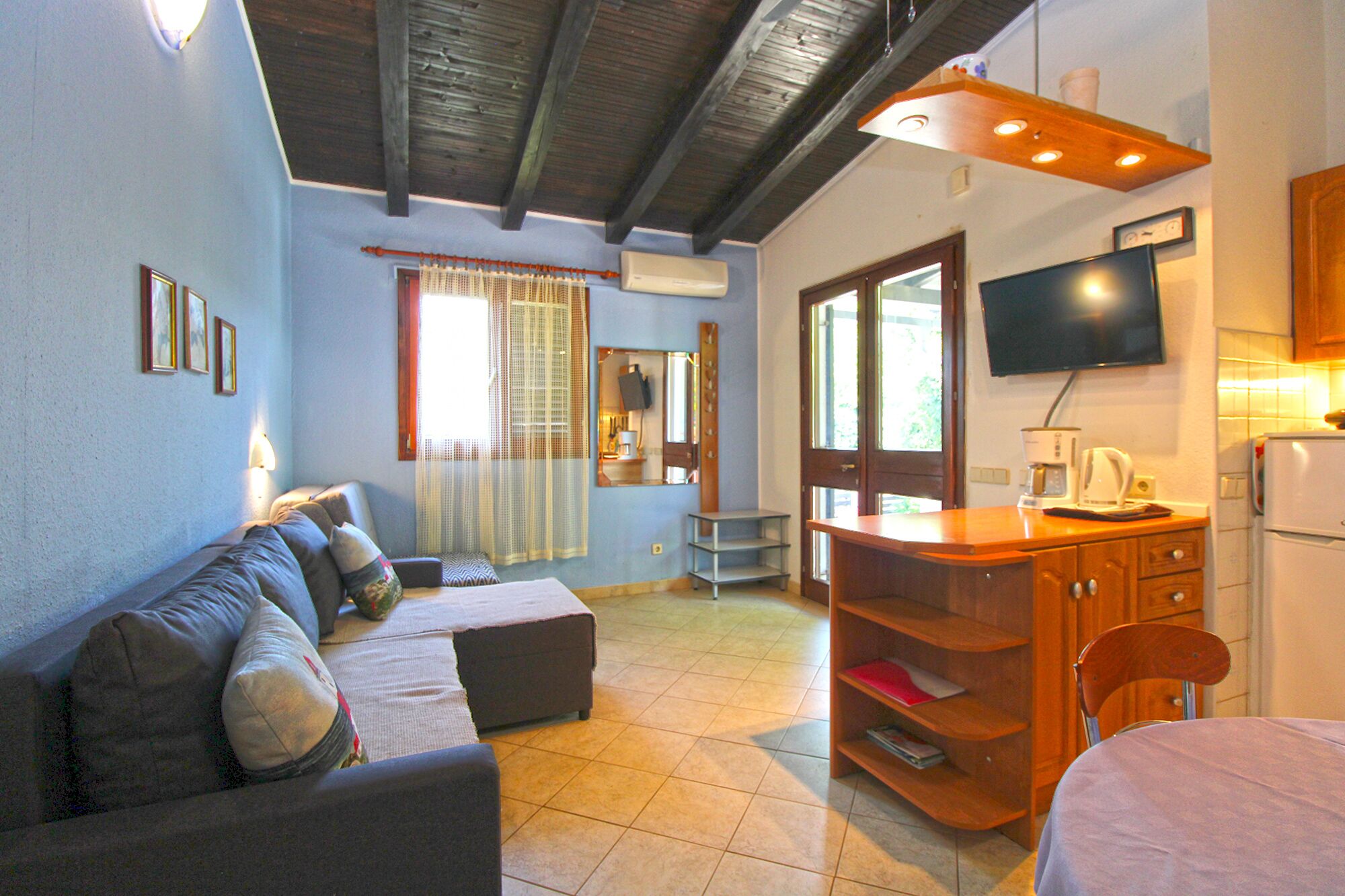 A room with a sofa, a small table, a television, and a refrigerator.