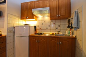 A kitchen with wooden cabinets, a white refrigerator, a gas stove, and a tiled backsplash. - Apartment 2435/208211 (Istria - Premantura), 450m from the beach (Premantura)