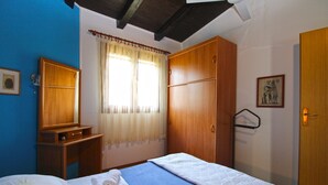 Ein Schlafzimmer mit einem Bett, einem Holzschrank, einem kleinen Nachttisch, einem Fenster mit Vorhängen und einer Tür.