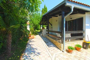 A pathway leading to a building with a covered porch, potted plants, and a trash bin. - Apartment 2435/208211 (Istria - Premantura), 450m from the beach (Premantura)