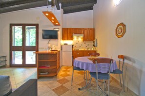 A kitchen with wooden cabinets, a refrigerator, a dining table with chairs, and a television mounted on the wall. - Apartment 2435/208211 (Istria - Premantura), 450m from the beach (Premantura)