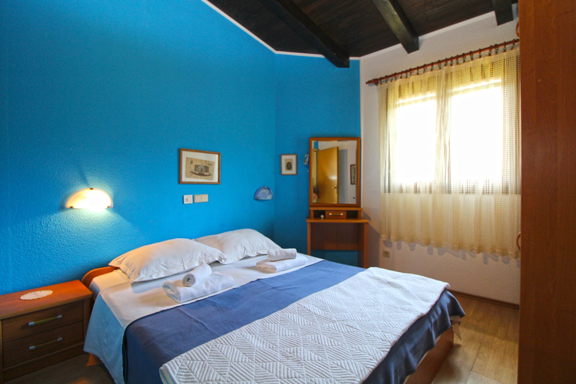 A bedroom with a bed, a nightstand, a mirror, and a wall-mounted light.