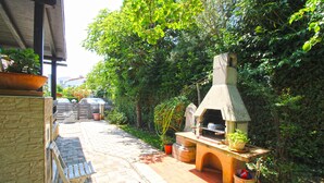 Eine Terrasse im Freien mit einem Stein-Barbecue, einem Holztisch und einem gepflasterten Weg.