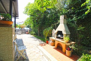 An outdoor patio with a stone barbecue grill, a wooden table, and a brick pathway. - Apartment 2435/208211 (Istria - Premantura), 450m from the beach (Premantura)