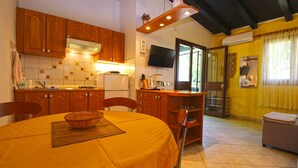 Una cocina con armarios de madera, una mesa de comedor con mantel amarillo y un televisor montado en la pared.