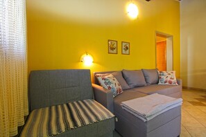 A living room with a grey sofa, a patterned ottoman, and a grey couch with floral cushions. There are two wall-mounted lights and two framed pictures on the wall. - Apartment 2435/208212 (Istria - Premantura), 450m from the beach (Premantura)