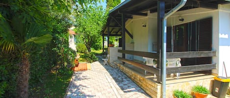 A pathway leading to a building with a covered porch, potted plants, and a trash bin.