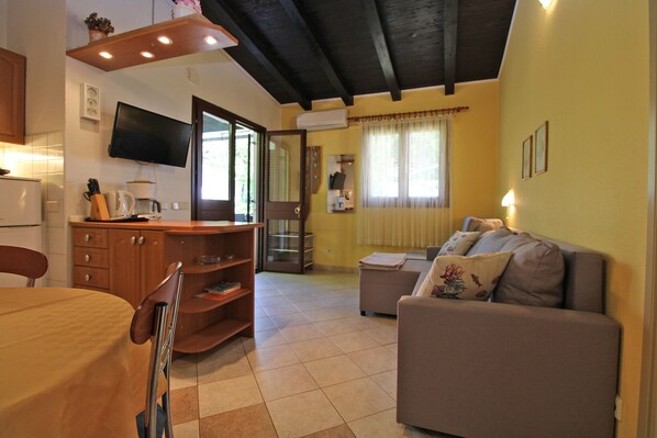 Un soggiorno con divano, tavolo da pranzo, angolo cottura e soffitto a travi a vista.