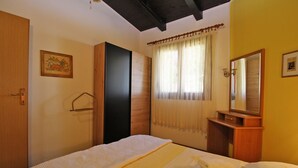 Un dormitorio con cama, armario de madera, espejo y ventana con cortinas.