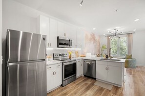 Una cocina moderna con electrodomésticos de acero inoxidable, armarios blancos y un amplio ventanal con cortinas.