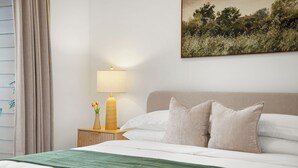 A neatly made bed with white linens, a green throw blanket, and two pillows. There is a nightstand with a lamp, a vase with flowers, and a candle. A painting of a landscape is on the wall. - King Bed + Balcony Walk to Ponce City Market & BeltLine in Atlanta (Atlanta)
